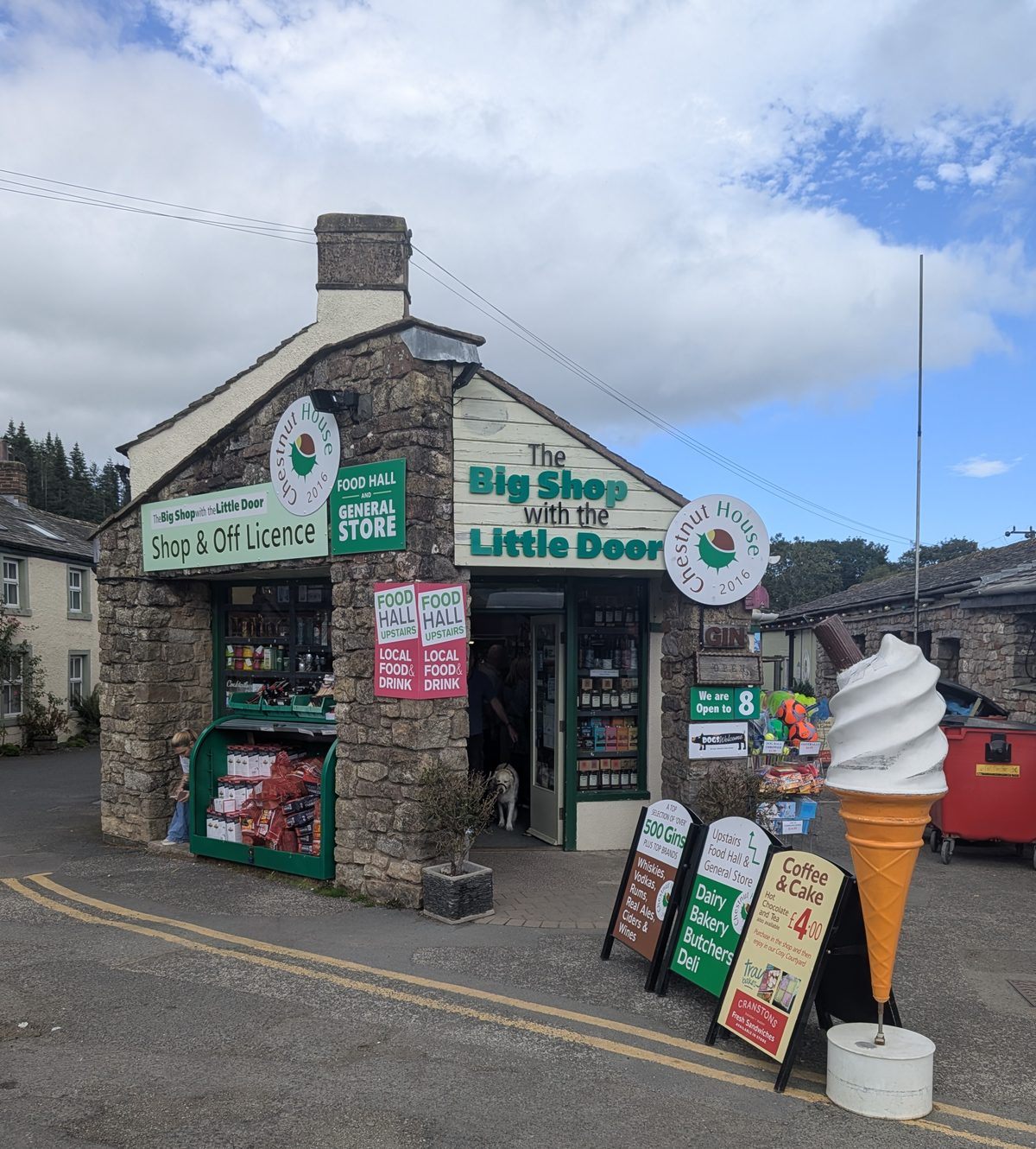 Chestnut House, a small stone-built shop and off-licence in Pooley Bridge signed 'The Big Shop with the Little Door', with A-boards and a large ice-cream cone outside