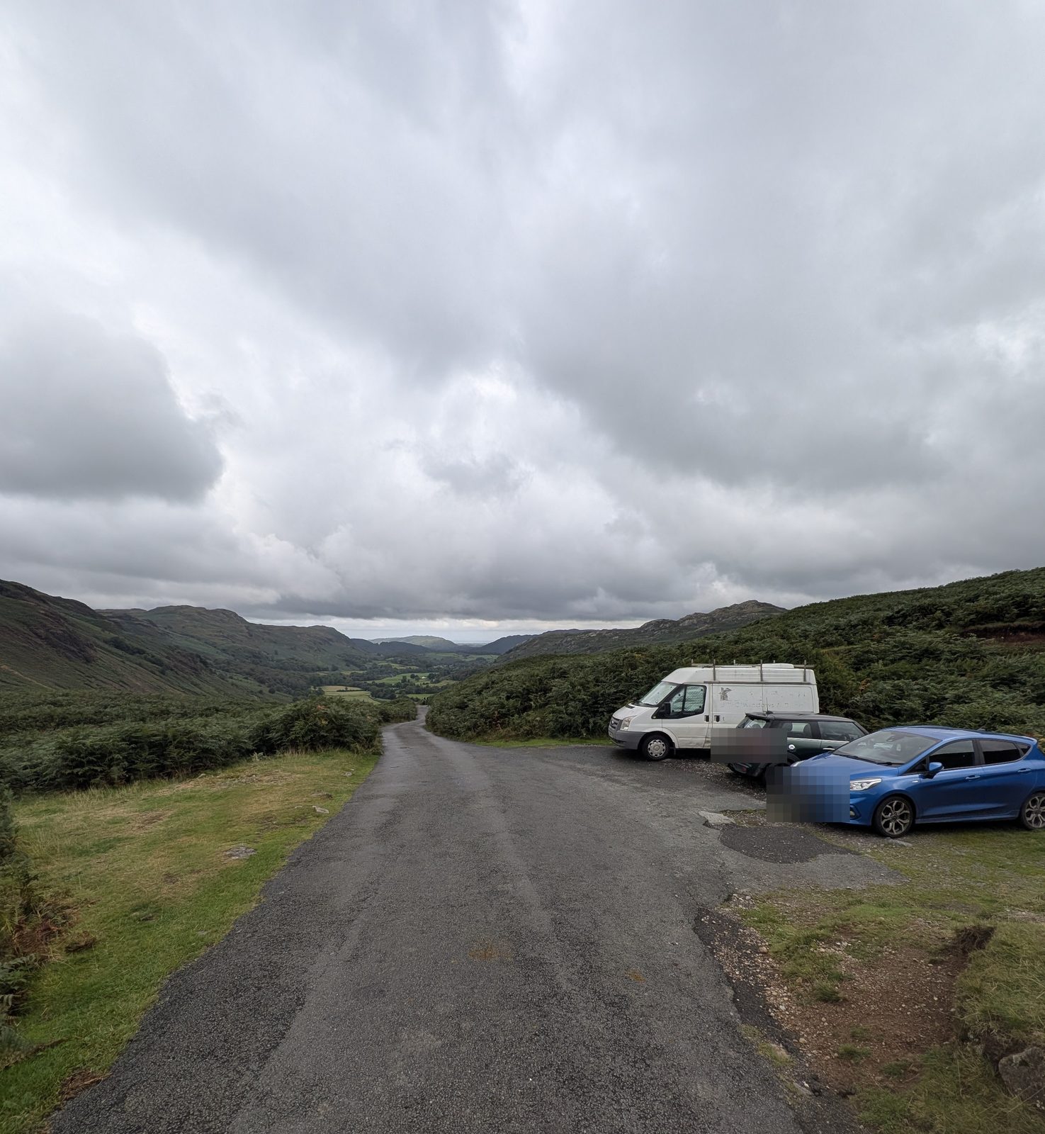 The lower parking area on the Hardknott Pass road below the fort, vehicles pulled in beside the tarmac with Eskdale beyond
