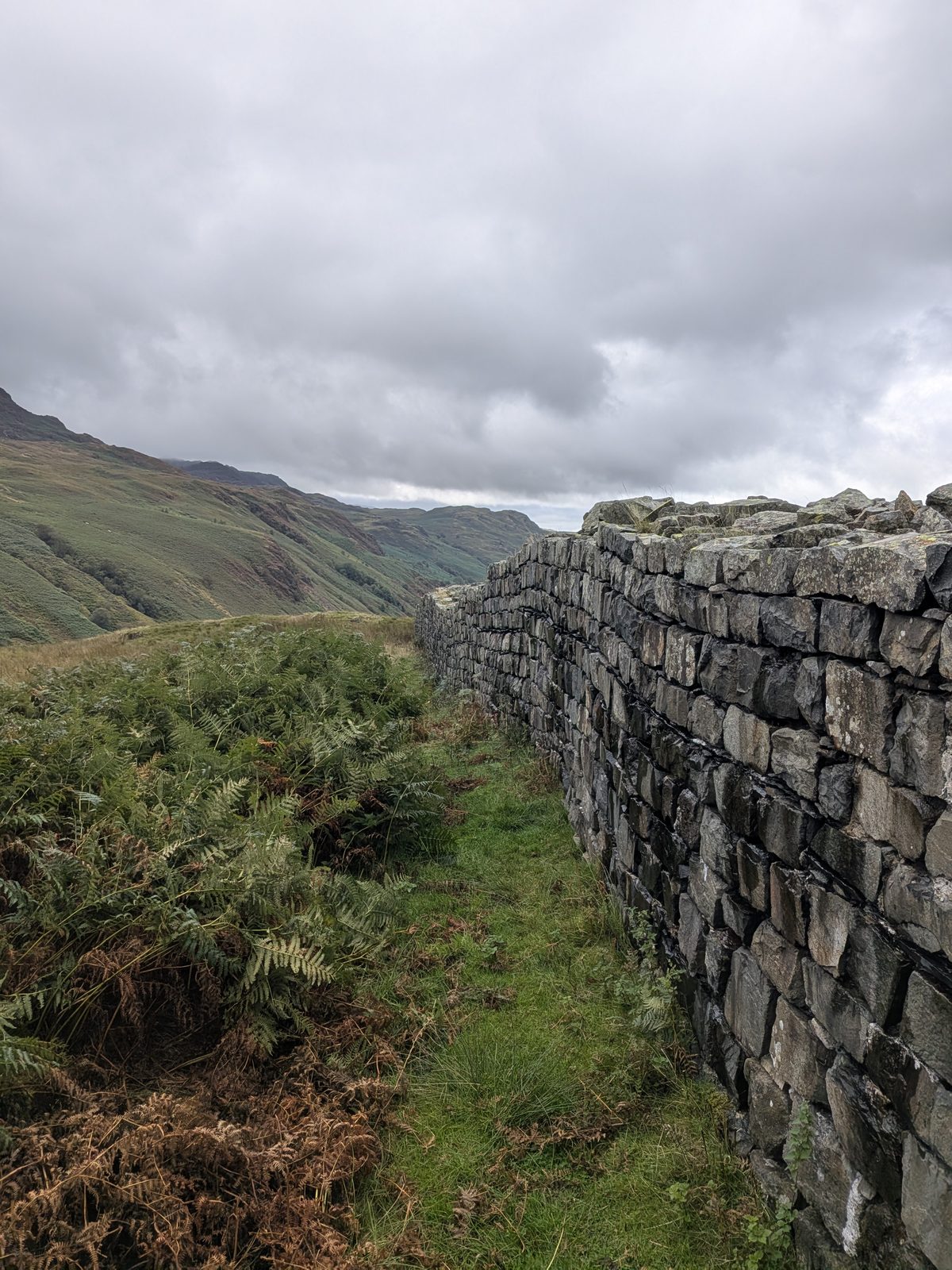 The outer wall of Hardknott Roman Fort standing head-high, with the fells of Eskdale beyond