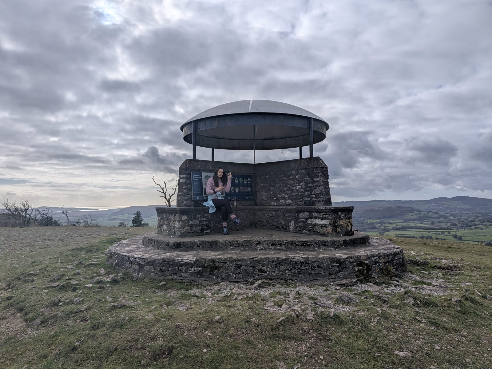The Mushroom shelter on top of Scout Scar, a round stone base under a domed metal roof, with Ellie sitting inside
