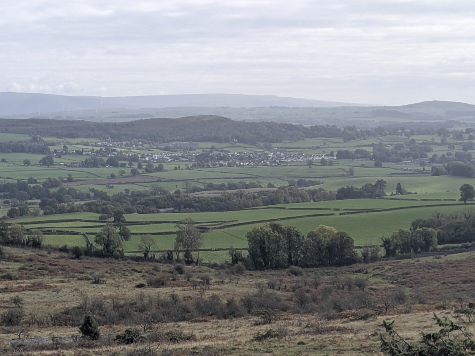 The view from Scout Scar over a green valley of walled fields to a village and the hills beyond