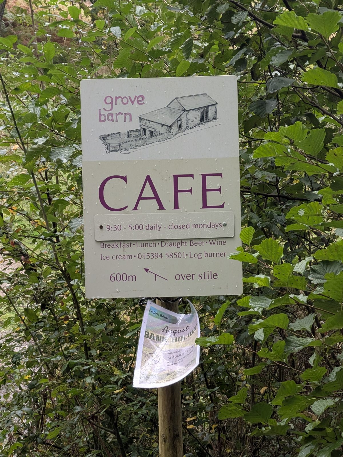 A Grove Barn café sign on a post among leaves, pointing 600 m over the stile