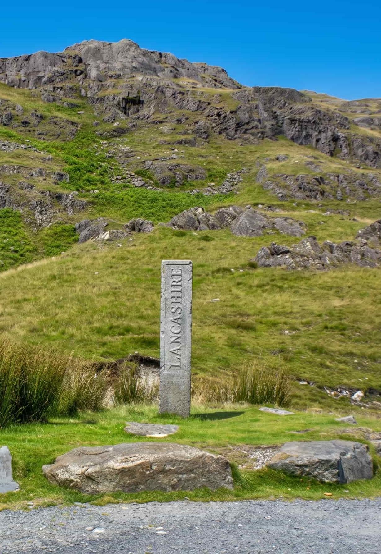 The Three Shire Stone at the summit of Wrynose Pass, inscribed Lancashire, with the fellside rising behind