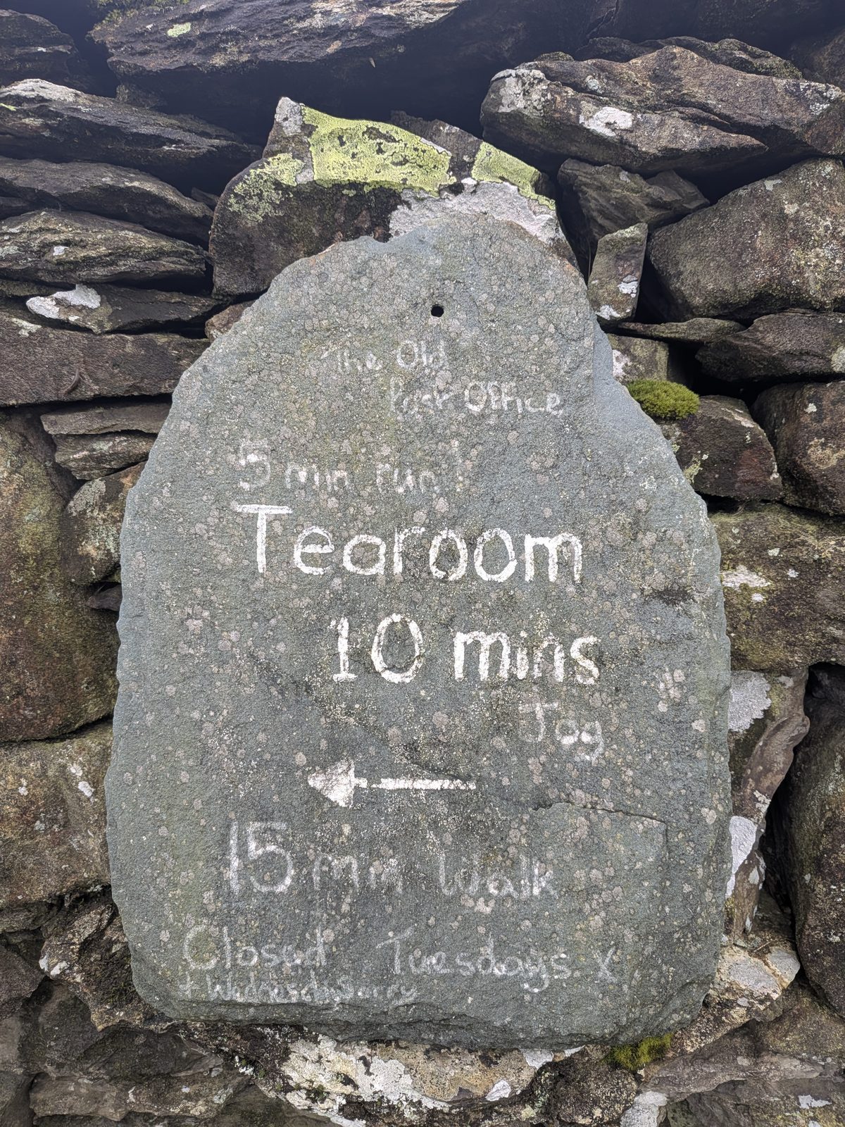 A slate sign set in a dry-stone wall, with hand-lettered directions to the Old Post Office tearoom