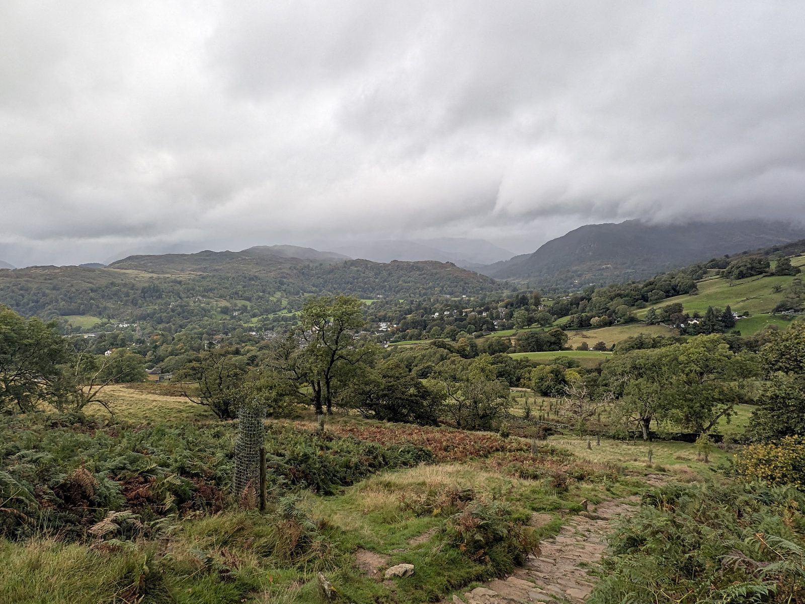 A view back over the valley under heavy cloud, with a flagged path in the foreground