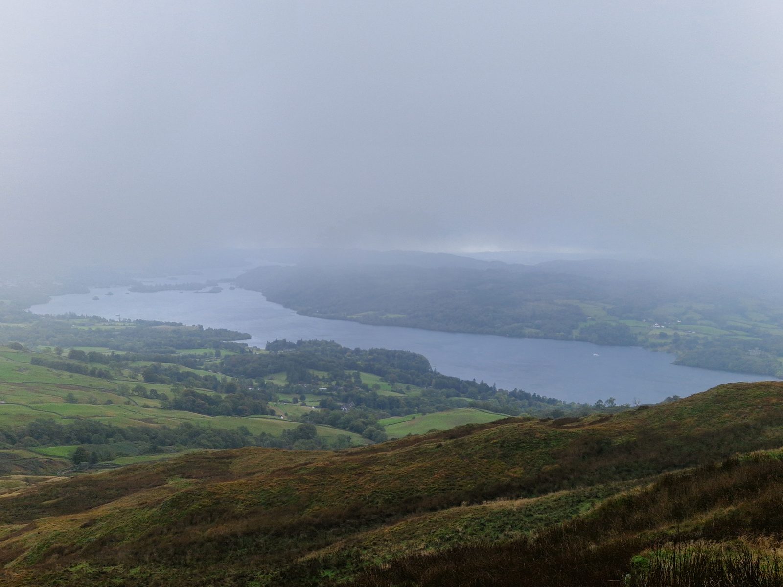 Windermere in the distance under heavy cloud, with brown hillside in the foreground