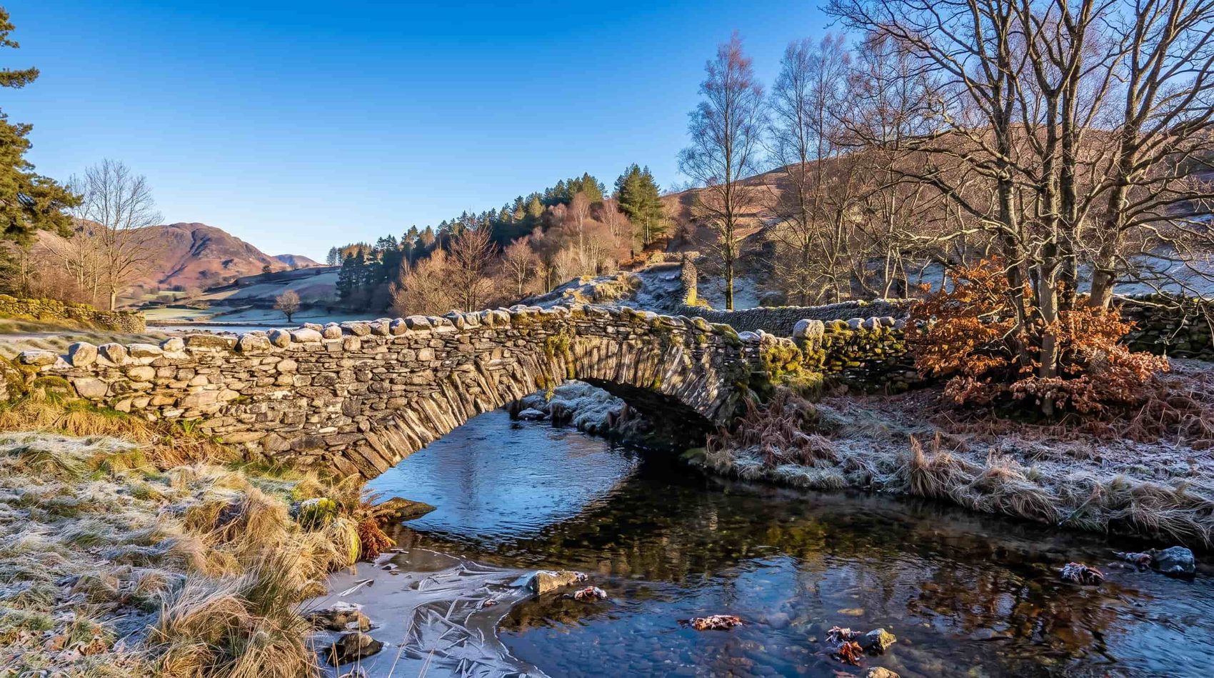The packhorse bridge over Watendlath Beck with the hamlet and tarn beyond, Borrowdale, Lake District