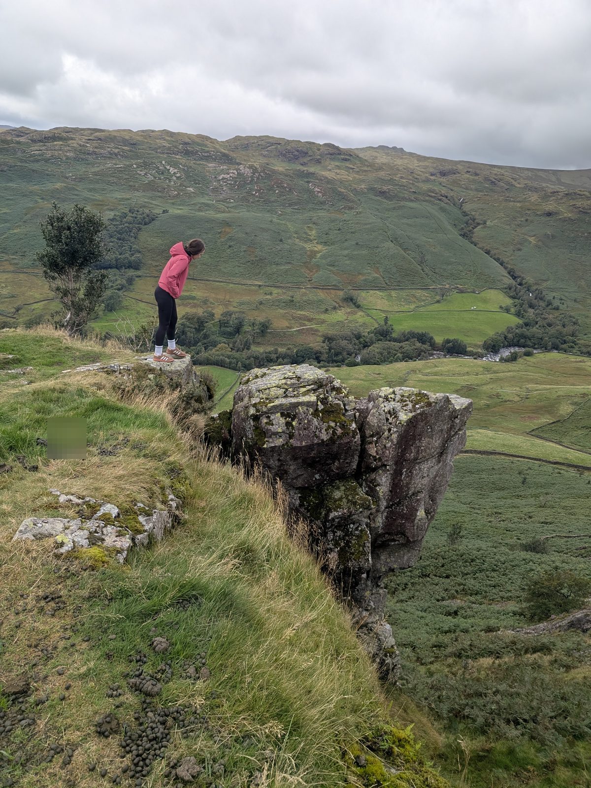 Wall footings on the western side of Hardknott Roman Fort under a low sky, with a walker beside them