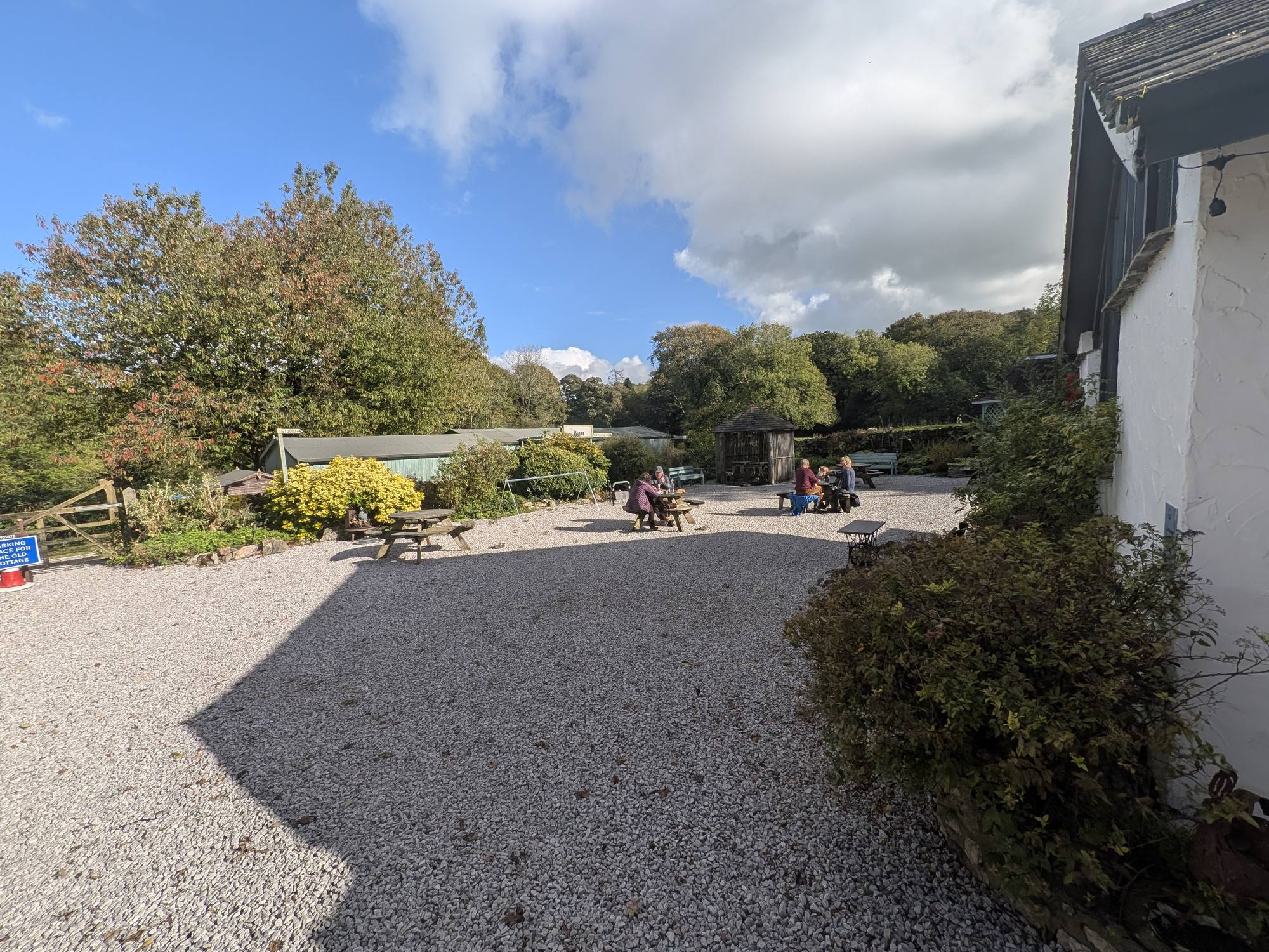 Gravel garden with picnic tables at The Wolf Cafe, Silverdale, with a long green timber building signed The Bau behind